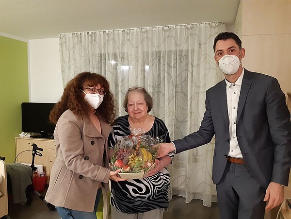 Bewohnerin, Angehörige und Einrichtungsleitung mit Obstkorb