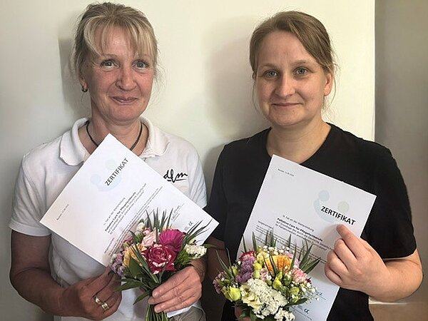 Zwei Personen mit Blumensträußen und Zertifikaten in den Händen