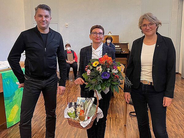 drei Menschen mit Blumen und Geschenk